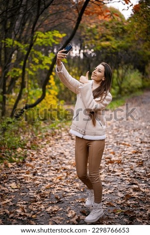 Woman taking selfie in autumn park. Young attractive lady using smartphone.