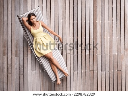 Young woman, sunbed and luxury summer resort, vacation or holiday to relax outdoors and lounge in the spring sun. Girl, sleeping on tanning bed and top view of modern wood deck in background Royalty-Free Stock Photo #2298782329