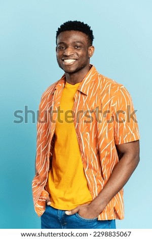 Authentic portrait of handsome smiling African American man wearing orange shirt isolated on blue background. Young stylish hipster model looking at camera posing for pictures. Summer concept 