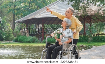 Senior couple and disabled wife in wheelchair with flower bouquet to watching nature view in park. 