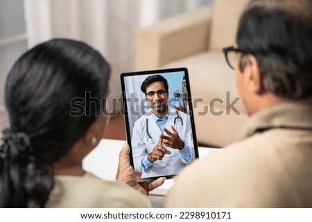 Shoulder shot of Indian Senior couple taking advice from doctor during online video call from tab at home - concept of remote health care, virtual consultation and ehealth Royalty-Free Stock Photo #2298910171