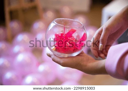 A woman holds a glass watering can with pink bows against a background of pink balloons.