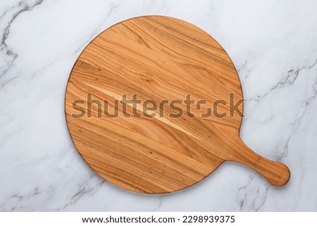 Round empty wooden charcuterie serving board with handle on a white or gray marble table, top view. Kitchenware, template with copy space. Flat lay design, mockup. Layout, cooking concept, frame. Royalty-Free Stock Photo #2298939375