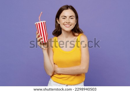 Young smiling happy cheerful fun cool woman 20s she wear yellow tank shirt hold cup of soda pop fizzy water look camera isolated on plain pastel light purple background studio People lifestyle concept