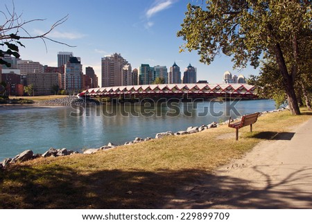 A pedestrian bridge across  Bow River in Calgary with skyscrapers in the background.