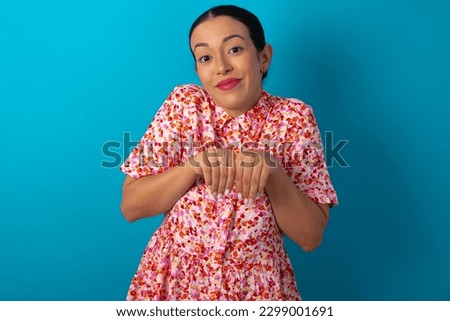 beautiful woman wearing floral dress over white studio background makes bunny paws and looks with innocent expression plays with her little kid