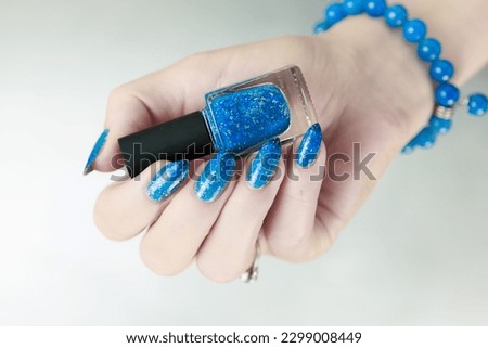 Woman's beautiful hand with long nails and blue manicure with bottles of nail polish