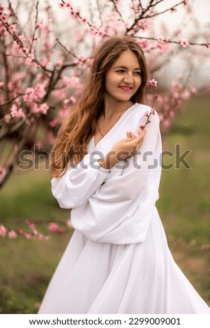 Woman peach blossom. Happy curly woman in white dress walking in the garden of blossoming peach trees in spring