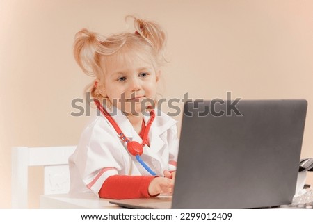 A little girl dressed as a doctor sits near a laptop.