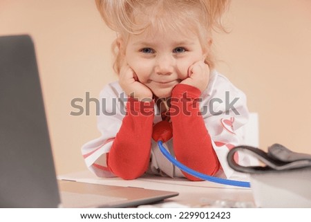 A little girl dressed as a doctor sits near a laptop.