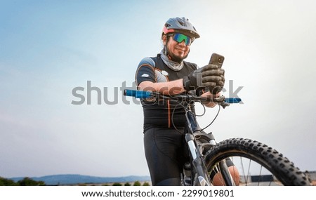 Male cyclist with helmet using cell phone. Cyclist on his bike texting with phone outdoors. cyclist man with helmet and glasses texting on cell phone outdoors