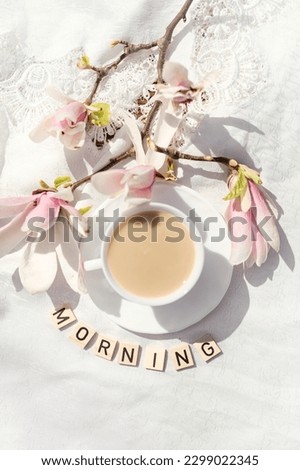 cup of coffee with milk and spring flowers magnolia branches against a white background. inscription morning. Top view, copy space. spring mood. good morning concept