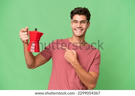 Young caucasian man holding coffee pot over isolated background and pointing it