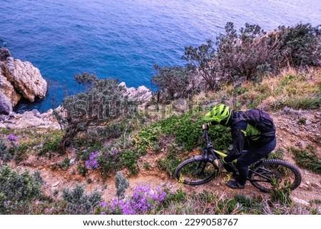 Unrecognisable mountain biker descends on a challenging trail steep towards the sea, Finale Ligure, Italy Royalty-Free Stock Photo #2299058767