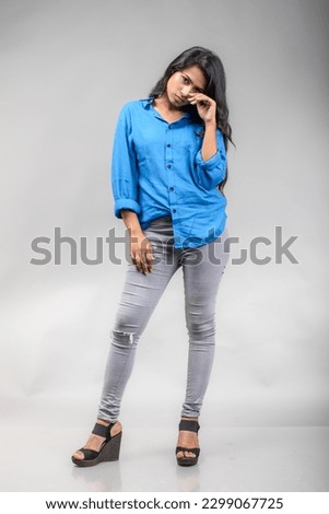Indian female young model in casual wear against grey background - stock photo. Long black hair model wearing blue shirt.