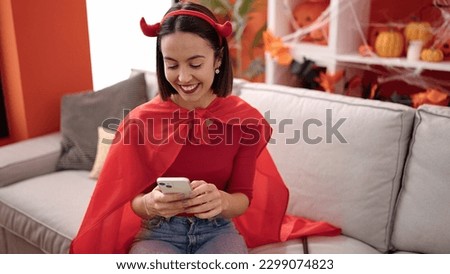 Young beautiful hispanic woman wearing devil costume using smartphone at home