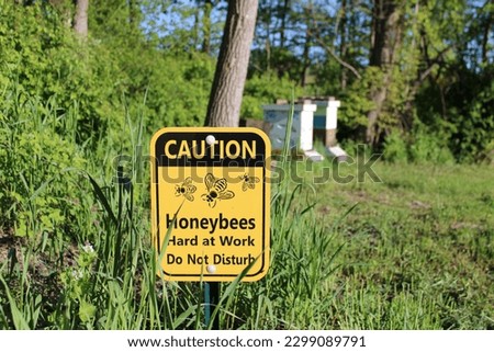 Caution Honey Bees Hard at Work Do Not Disturb sign with hives in the background