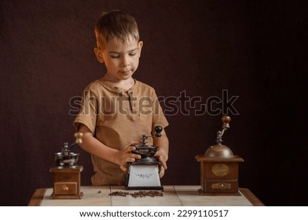 A little boy looks at the old coffee grinders on the table. Portrait on a brown background