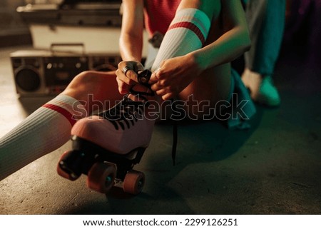 A young girl is sitting on the ground outdoors tying the shoe laces on her retro styled roller skates. Royalty-Free Stock Photo #2299126251