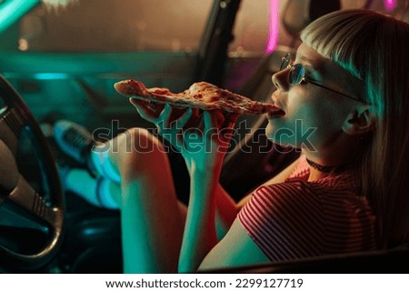 A retro girl with roller skates is sitting in the front seat of the car enjoying pizza.