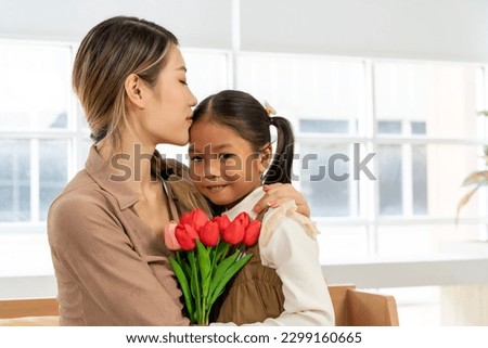 Asian young mother kiss on forehead of lovely daughter after receives bouquet of flowers tulips at home, Happy family holiday and togetherness. Mother's day concept.