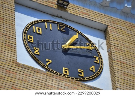 close photo of a black dial on a brick tower with golden hands and numbers.
