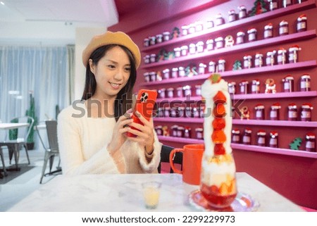 Woman use mobile phone to take photo of her tower of strawberry dessert in restaurant