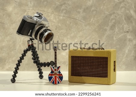 A photo of a camera playing electric guitar with a yellow amplifier on the background with white background texture 