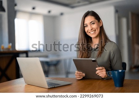 Smiling confident businesswoman looking at camera sitting at home office desk. Modern stylish female manager, successful female entrepreneur holding digital tablet posing for business portrait.
 Royalty-Free Stock Photo #2299269073