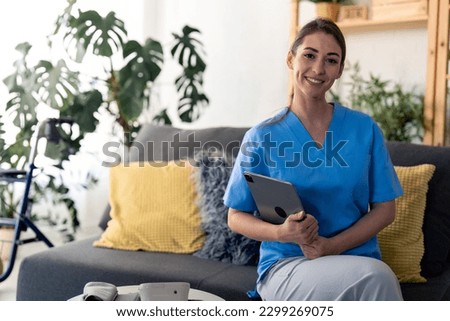 Young confident nurse looking at camera, holding digital tablet, posing for portrait photo at work in nursing home. Portrait of satisfied female home care worker. Smiling healthcare professional. Royalty-Free Stock Photo #2299269075