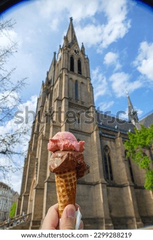 Pink and brown ice cream in the cone in front of the church. Church of St. Ludmila in Prague Vinohrady district.  Artistic shot with upper vignetting for social media presentation of food desert. 