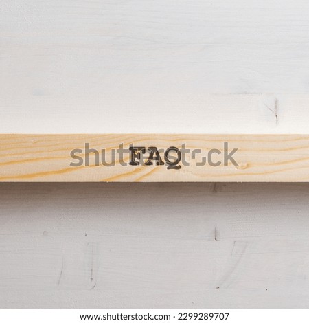 Wooden slat with a FAQ sign on it placed over plain simple wooden background. With plenty of copy space.