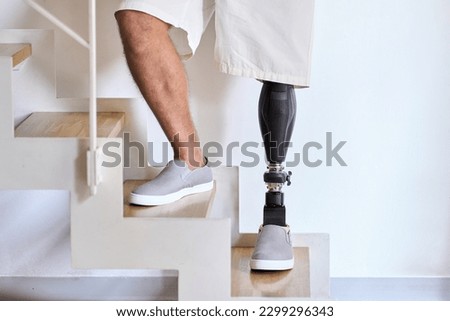 Man amputee with prosthetic leg disability on above knee transfemoral leg prosthesis artificial device stands on feet on stairs, close up. People with amputation disabilities everyday life. Royalty-Free Stock Photo #2299296343
