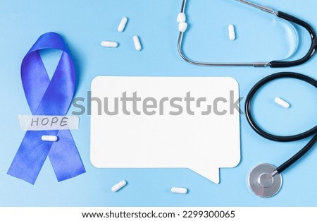 One blue ribbon with sticky tape with the word: hope, stethoscope,empty callout and scattered pills on a blue background with copy space,flat lay closeup.Concept for world cancer day,abdominal disease