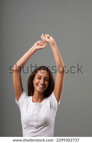 Dance or great joy and frenzy with raised arms. Emotional portrait of a young woman isolated on a neutral background. Long brown hair, slim, white shirt. State of mind concept Royalty-Free Stock Photo #2299302737