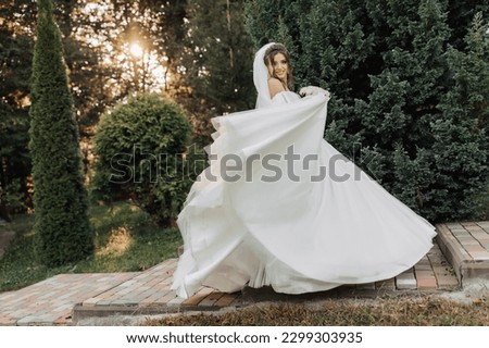 Wedding photo. The bride in a voluminous white dress and a long veil, smiling, twirling with a bouquet of white roses, holding her dress. Portrait of the bride. Beautiful makeup and hair.