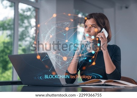 Pensive attractive beautiful businesswoman in formal wear working on laptop at office workplace in background. Using phone. Concept of business education, blockchain cryptocurrency technology.