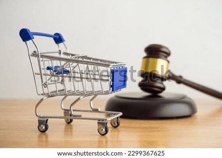 Shopping trolley cart and hammer judge gavel on wooden table with white wall background copy space. Consumer rights and and responsibilities to safety, customer protection, commercial law concept. Royalty-Free Stock Photo #2299367625