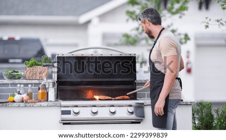 Hispanic man cooking on barbecue in the backyard. Chef preparing barbecue. Barbecue chef master. Man in apron preparing delicious grilled barbecue food, bbq meat. Grill and barbeque. Royalty-Free Stock Photo #2299399839
