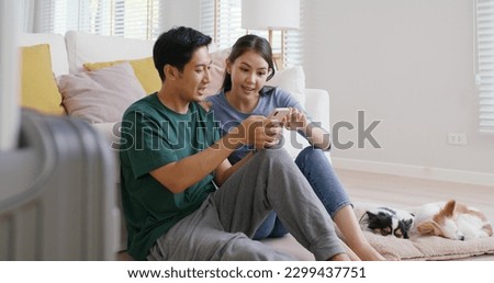Asia people young family man woman smile happy fun laugh look at phone sit at home pay for hotel booking, search choose, buy ticket on social media app for budget travel abroad trip getaway plan tour. Royalty-Free Stock Photo #2299437751