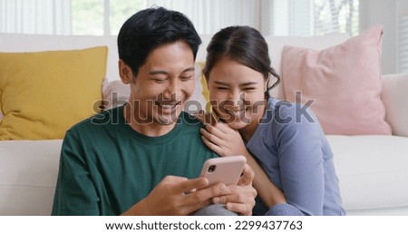 Asia people young family man woman smile happy fun laugh look at phone sit at home pay for hotel booking, search choose, buy ticket on social media app for budget travel abroad trip getaway plan tour. Royalty-Free Stock Photo #2299437763
