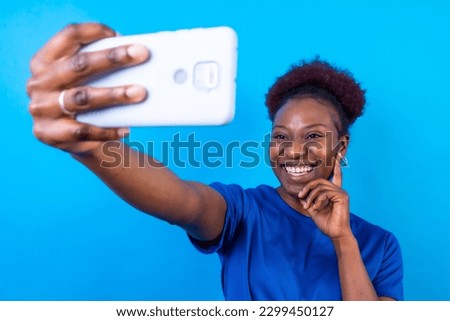 Young african american woman isolated on a blue background smiling and making a selfie, studio shoot