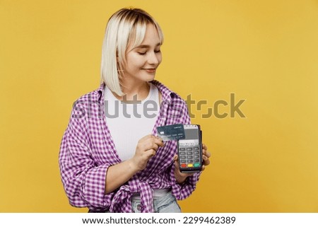 Young blonde woman 20s she wear pink tied shirt white t-shirt hold wireless modern bank payment terminal to process acquire credit card isolated on plain yellow background. People lifestyle concept
