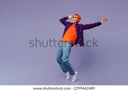 Full body young man of African American ethnicity wear casual shirt orange hat stand on toes leaning back with outstretched hand dance isolated on plain pastel purple color background studio portrait