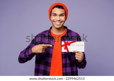 Young man of African American ethnicity wear casual shirt orange hat hold point finger on gift certificate coupon voucher card for store isolated on plain pastel light purple color background studio