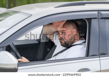 Overweight man drives in car without air conditioning in hot summer weather. Male wiping sweat from forehead suffering from heat stuffiness. Broken air conditioner. Tired exhausted overheated man. Royalty-Free Stock Photo #2299469903