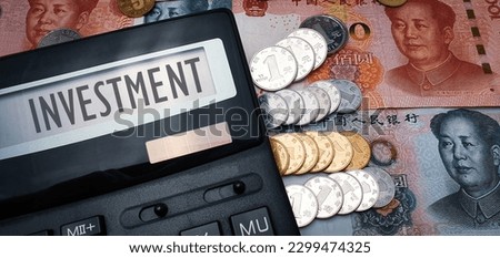 The word "investment" on calculator screen, Chinese currency and coins in the background. Illustration Chinese investment in global economy Royalty-Free Stock Photo #2299474325
