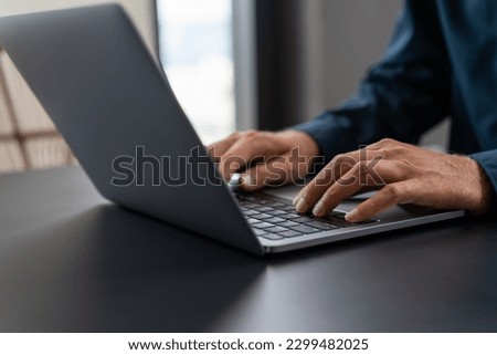 Hands of unrecognizable businessman in blue shirt using laptop computer at black table. Concept of technology and communication