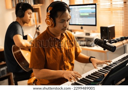 Group of Asian men making music at home studio. He plays guitar and keyboard.