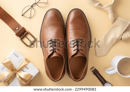 Top view layout. Honor Dad's sophistication with leather shoes, necktie, wristwatch, glasses, belt, giftbox with ribbon bow, coffee cup, men's accessories on a beige background Royalty-Free Stock Photo #2299490081